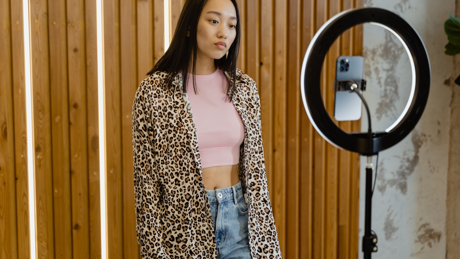 woman in leopard print blouse filming herself using a selfie light and phone