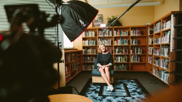 small business owner sitting in front of a bookshelf being filmed for video marketing video